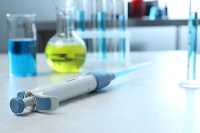 Laboratory analysis. Micropipette and different glassware with liquids on light grey marble table, closeup. Space for text