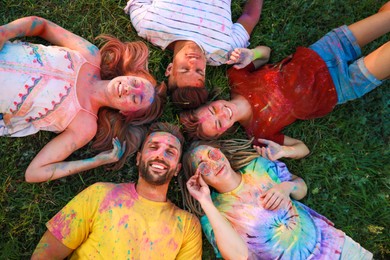 Photo of Happy friends covered with colorful powder dyes on green grass outdoors, above view. Holi festival celebration