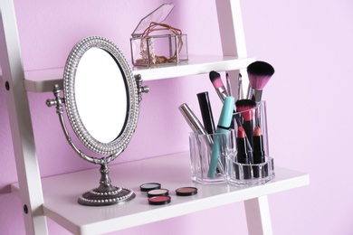 Photo of Organizer with cosmetic products for makeup on shelf near color wall
