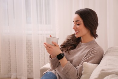 Photo of Young woman with smart watch and cup of drink at home, space for text