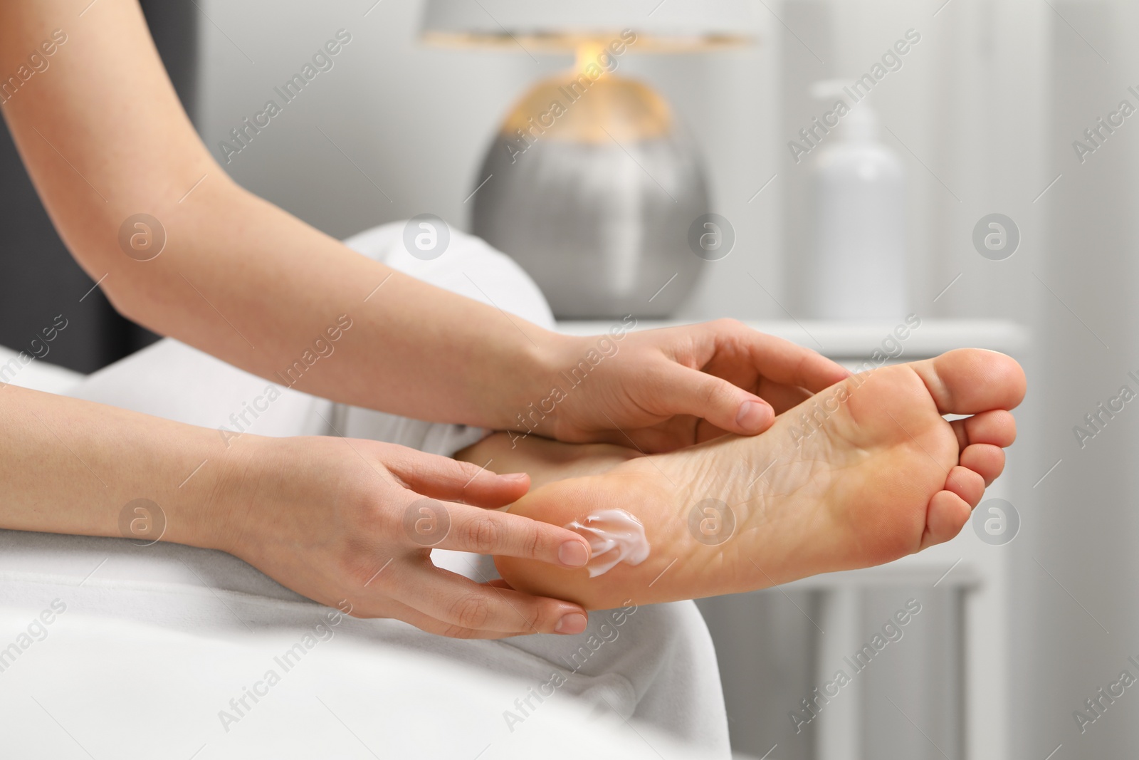Photo of Young woman with dry skin applying cream onto her foot indoors, closeup