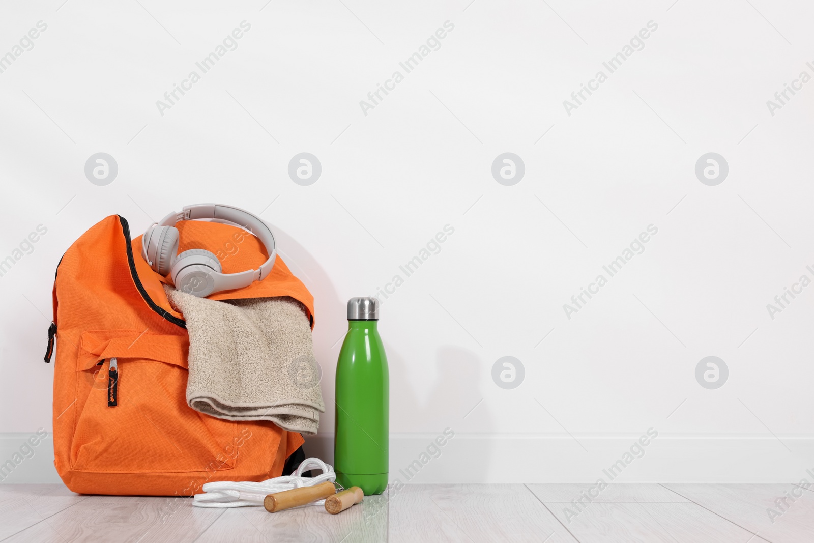 Photo of Backpack and sports equipment on floor near white wall, space for text