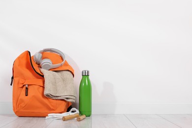 Photo of Backpack and sports equipment on floor near white wall, space for text