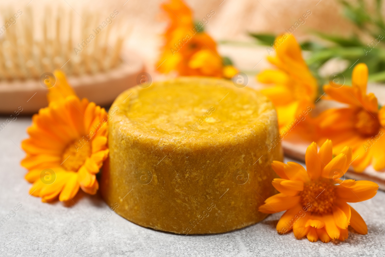 Photo of Yellow solid shampoo bar and flowers on light table, closeup. Hair care