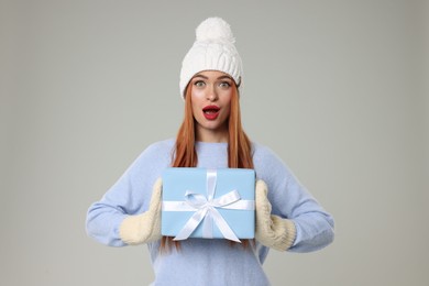 Photo of Emotional young woman in hat and sweater with Christmas gift on light grey background