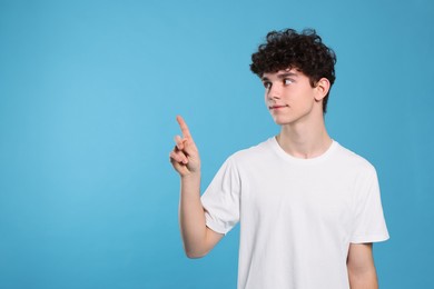 Photo of Teenage boy pointing at something on light blue background. Space for text
