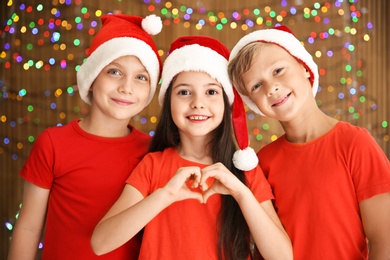 Cute little children in Santa hats on blurred lights background. Christmas celebration