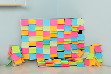 Photo of Computer and speakers covered with sticky notes on table in office. April Fool's Day celebration