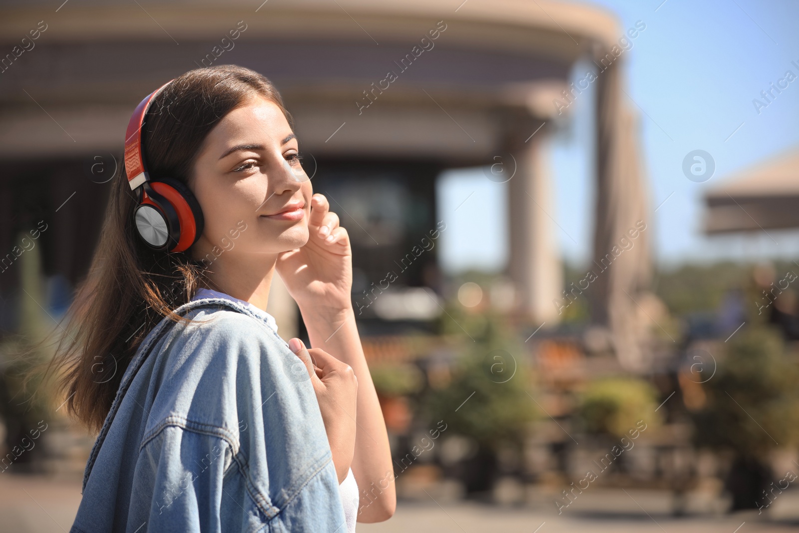 Photo of Young woman with headphones listening to music outdoors. Space for text