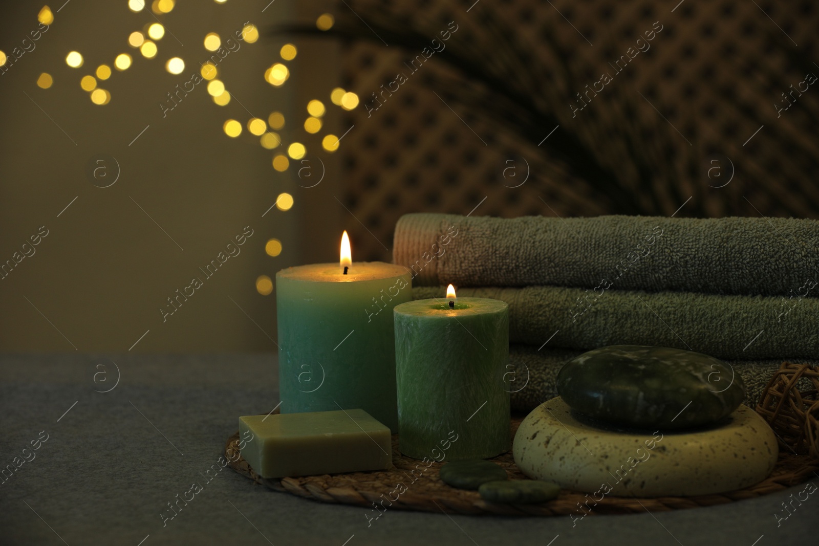 Photo of Spa composition. Burning candles, stones, soap and towels on grey table, space for text