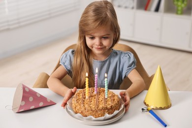 Photo of Cute girl with birthday cake at table indoors