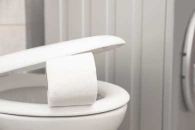 Photo of Toilet bowl with paper roll in bathroom. Space for text