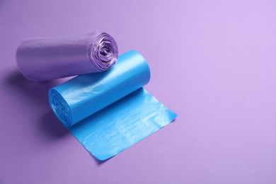 Rolls of different color garbage bags on violet background. Space for text