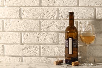 Photo of Bottle and glass of wine on white marble table near brick wall. Space for text