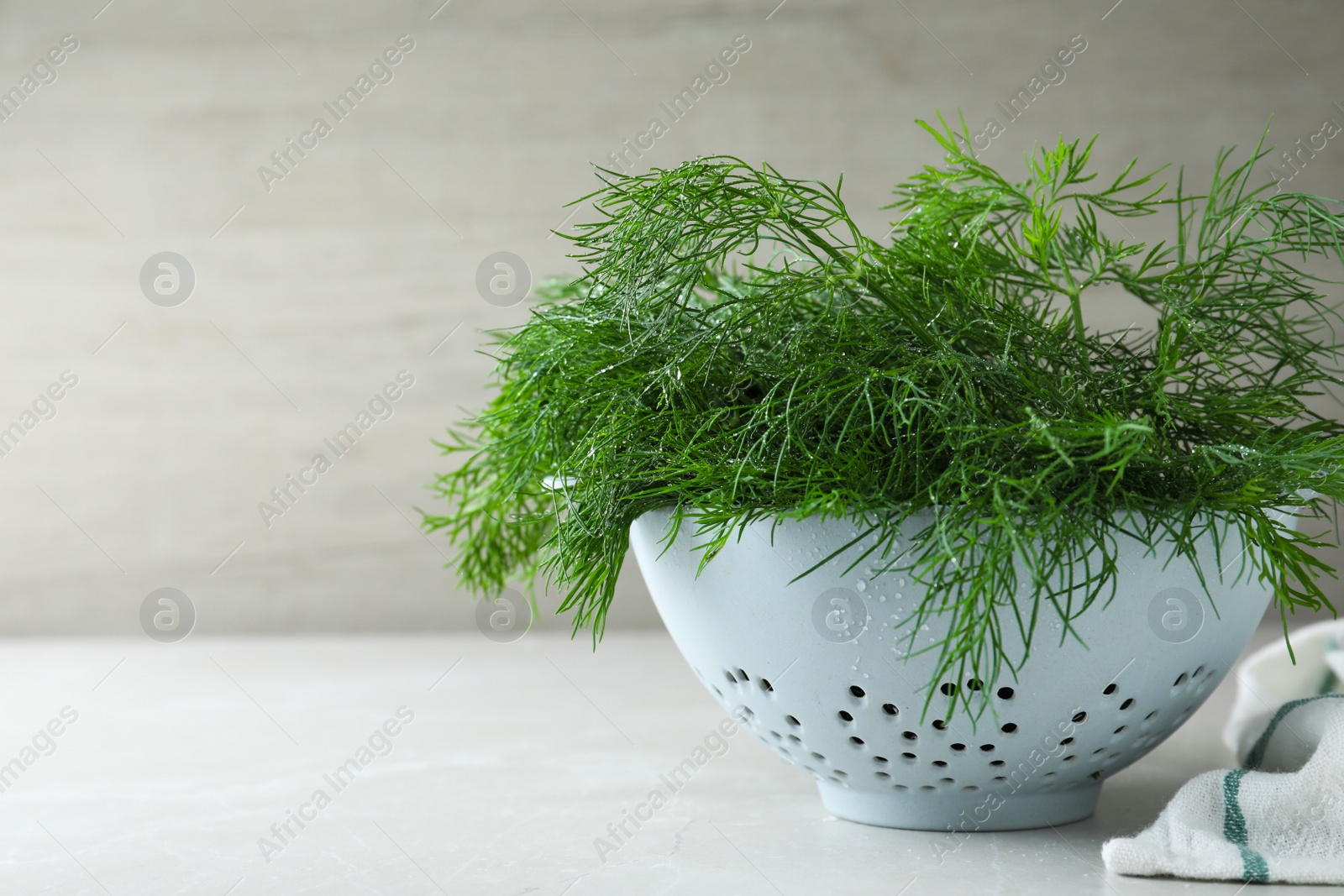 Photo of Fresh dill in colander on white table, space for text