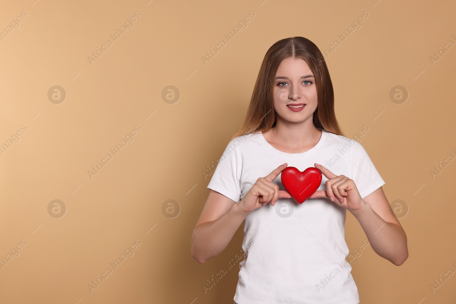 Photo of Young woman holding red heart on beige background, space for text. Volunteer concept
