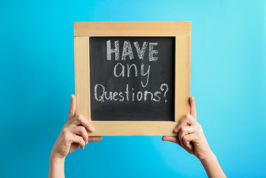 Woman holding blackboard with phrase HAVE ANY QUESTIONS on blue background, closeup