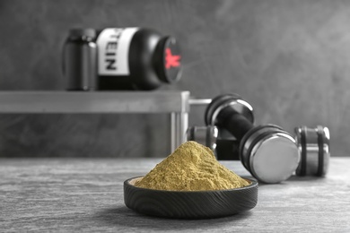 Hemp protein powder in bowl and dumbbells on table. Space for text