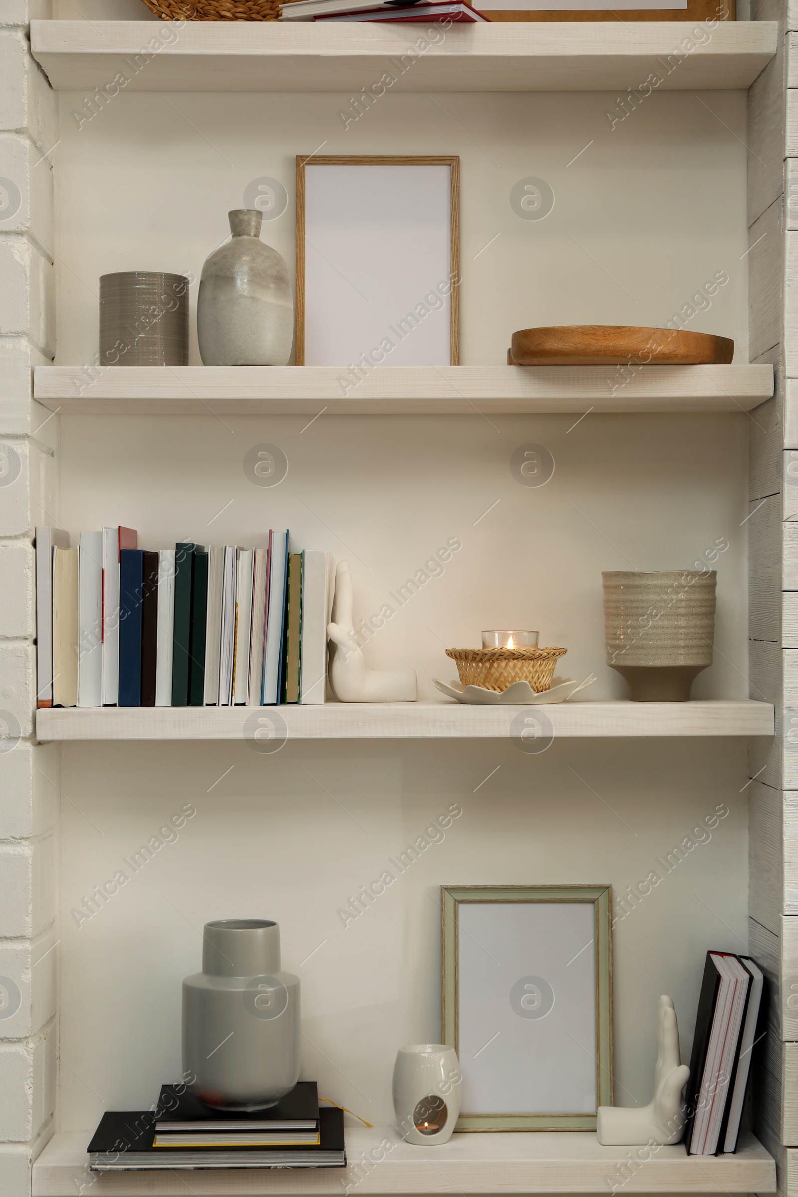 Photo of Books, empty frames and different decor on shelves indoors. Interior design