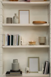 Photo of Books, empty frames and different decor on shelves indoors. Interior design