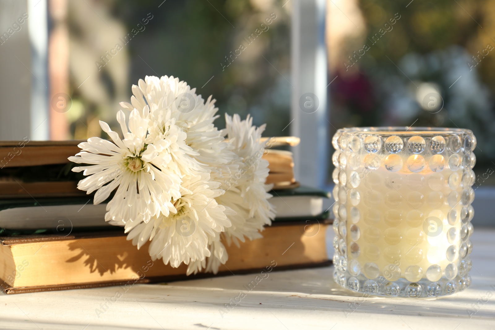 Photo of Book with beautiful chrysanthemum flowers as bookmark and candle on white table