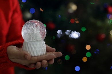 Woman holding snow globe on blurred background, closeup. Space for text