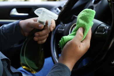 Photo of Man cleaning steering wheel with rag and spray bottle in car, closeup