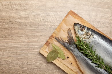 Photo of Board with salted herrings and bay leaves on wooden table, top view. Space for text