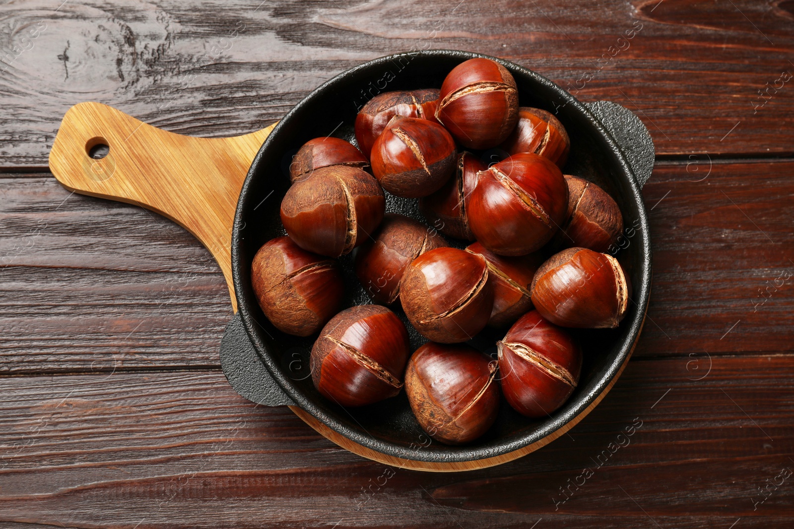 Photo of Roasted edible sweet chestnuts in baking dish on wooden table, top view