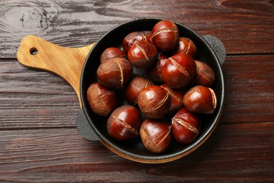 Roasted edible sweet chestnuts in baking dish on wooden table, top view