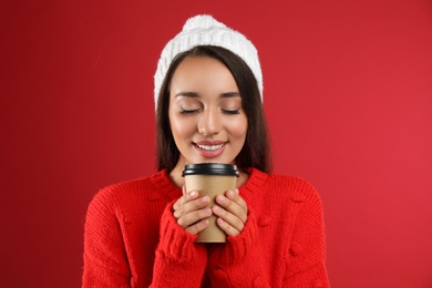 Happy beautiful woman with paper cup of mulled wine on red background