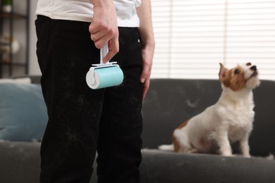 Photo of Pet shedding. Man with lint roller removing dog's hair from pants at home, closeup