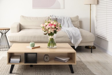 Photo of Beautiful bouquet of fresh flowers in vase on wooden coffee table indoors