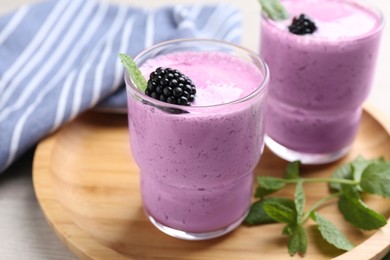 Delicious blackberry smoothie in glasses on wooden tray, closeup