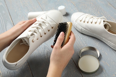 Woman cleaning stylish footwear on grey wooden background, closeup. Shoe care accessories