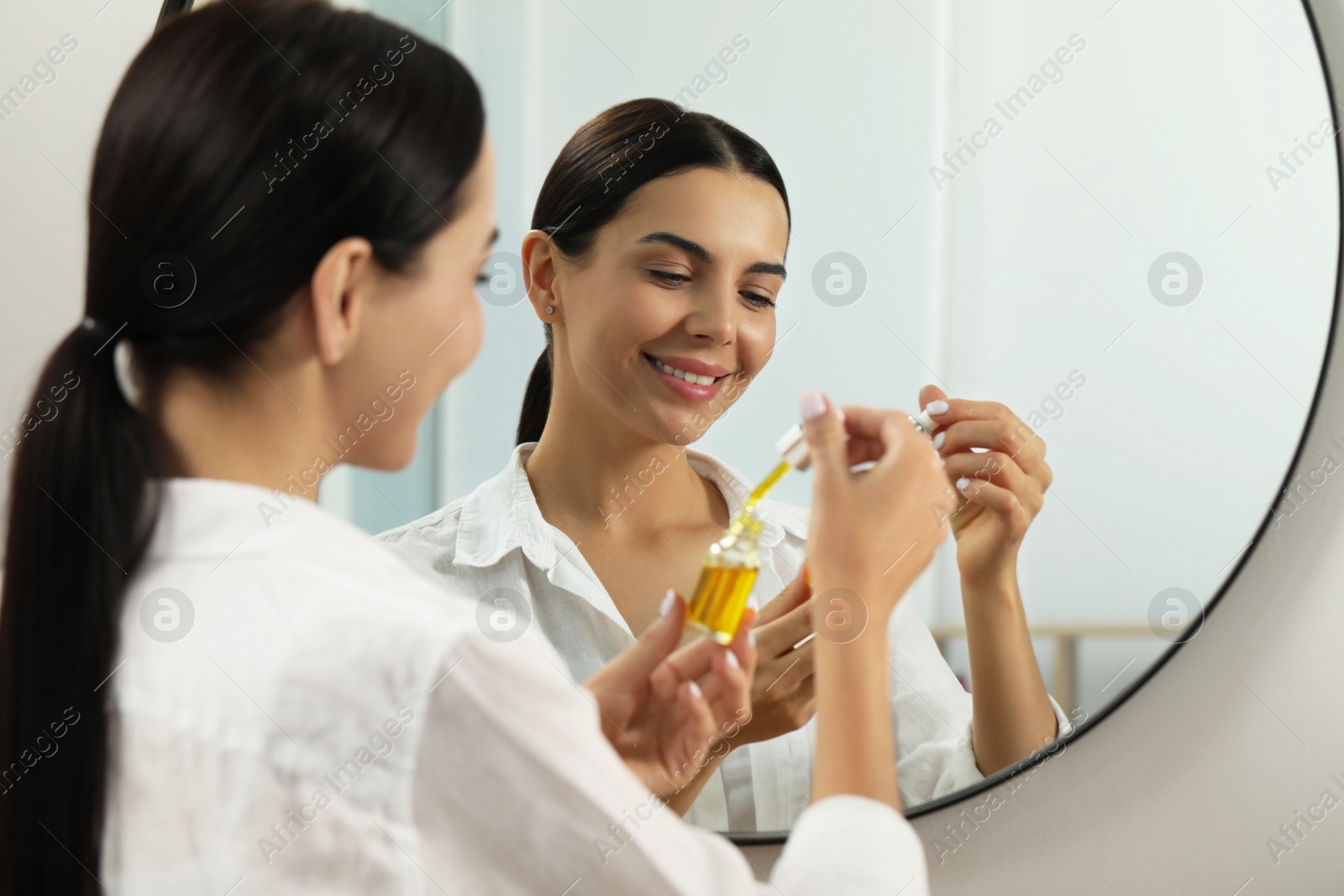 Photo of Young woman with bottle of essential oil near mirror
