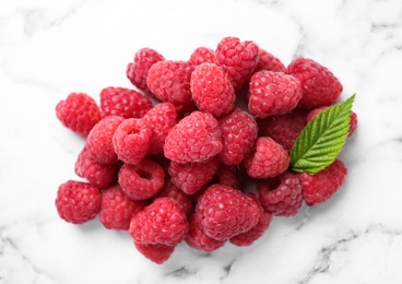 Photo of Delicious fresh ripe raspberries with green leaf on white marble table, above view