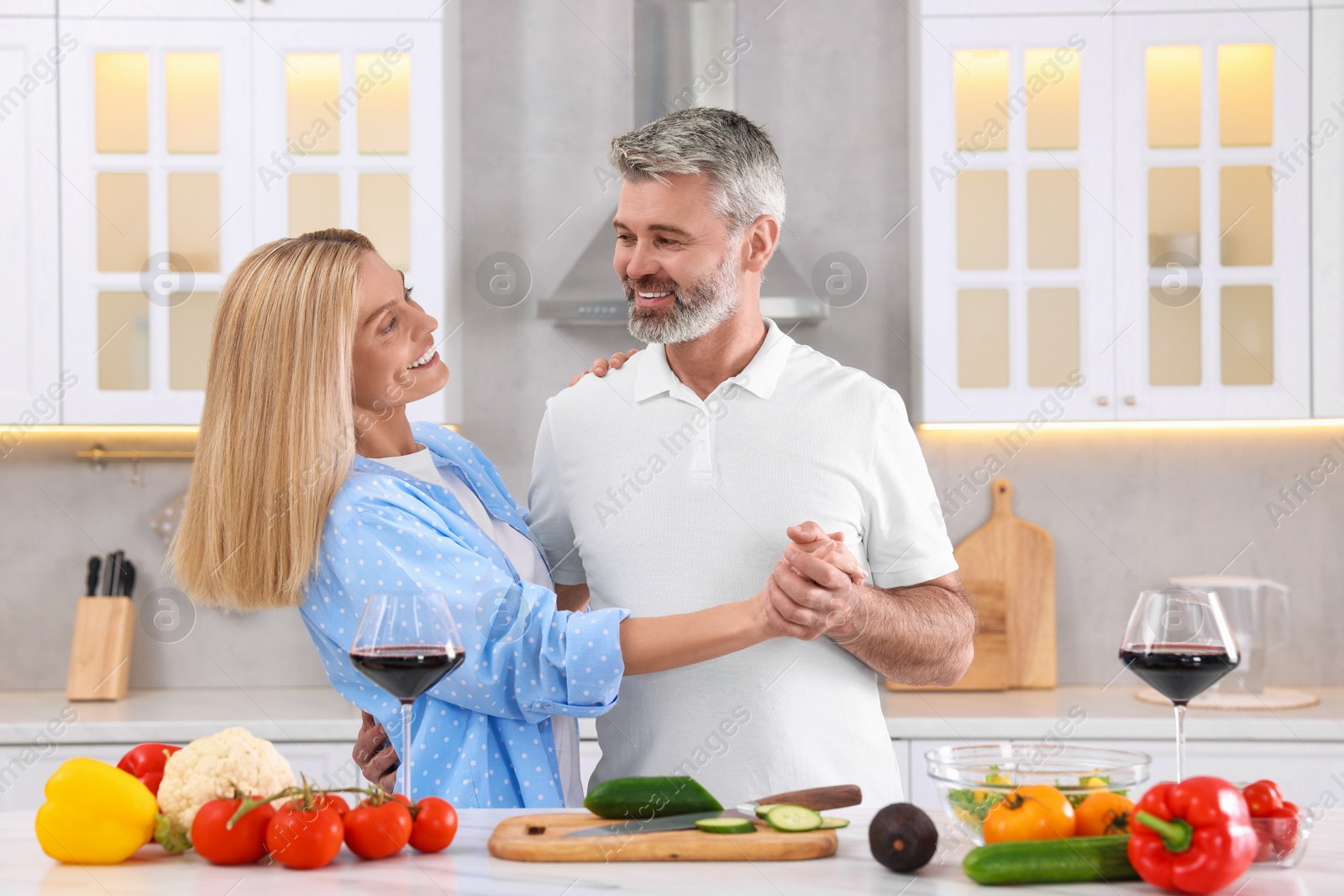 Photo of Happy affectionate couple cooking together at white table in kitchen