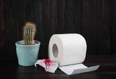 Photo of Roll of toilet paper and cactus on black wooden table. Hemorrhoid problems