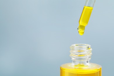Photo of Dripping yellow serum from pipette into bottle on grey background, closeup. Space for text