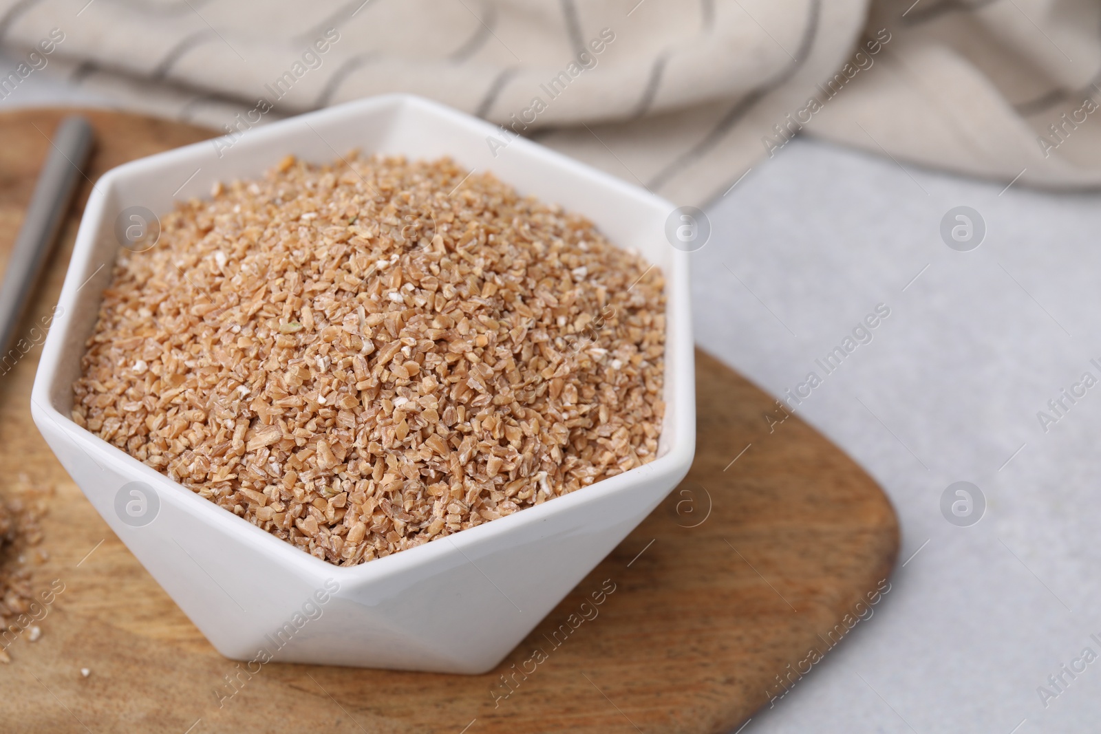 Photo of Dry wheat groats in bowl on light table, closeup. Space for text