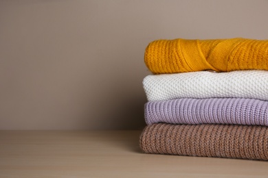 Photo of Stack of folded knitted sweaters on wooden table. Space for text