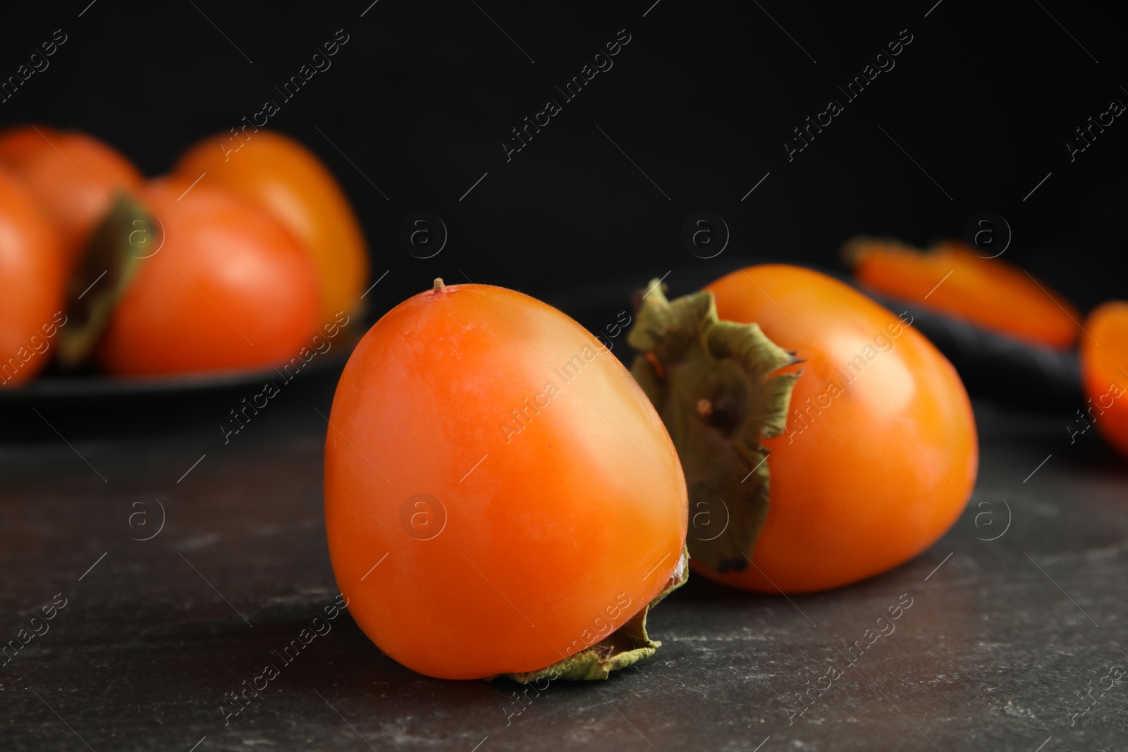 Photo of Tasty ripe persimmons on black slate table, closeup