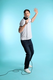Photo of Handsome man in casual clothes singing with microphone on color background