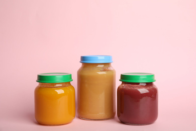 Jars with healthy baby food on pink background