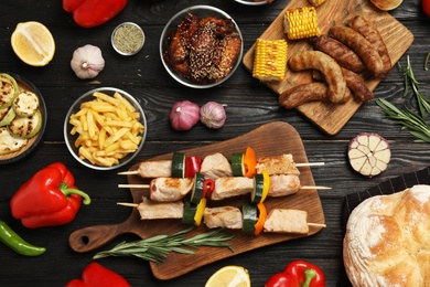 Photo of Flat lay composition with barbecued meat and vegetables on black wooden table