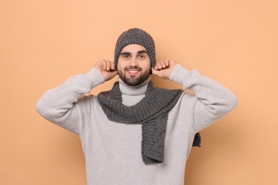 Smiling man in knitted scarf and hat on beige background