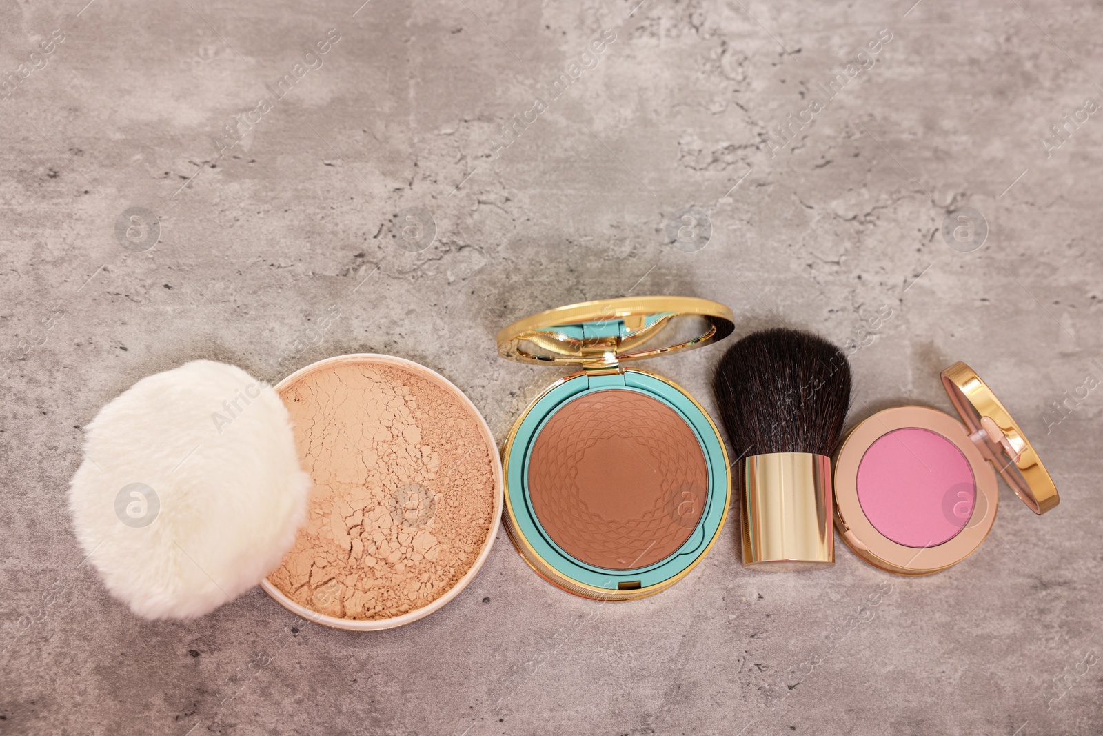 Photo of Bronzer, powder, blusher and brush on grey textured table, flat lay