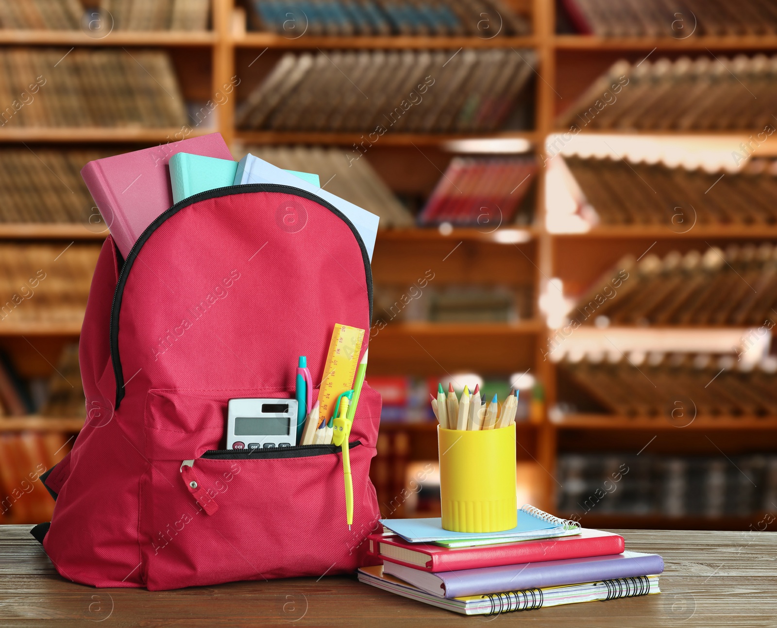 Image of Backpack with school stationery on wooden table in library