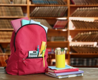 Backpack with school stationery on wooden table in library